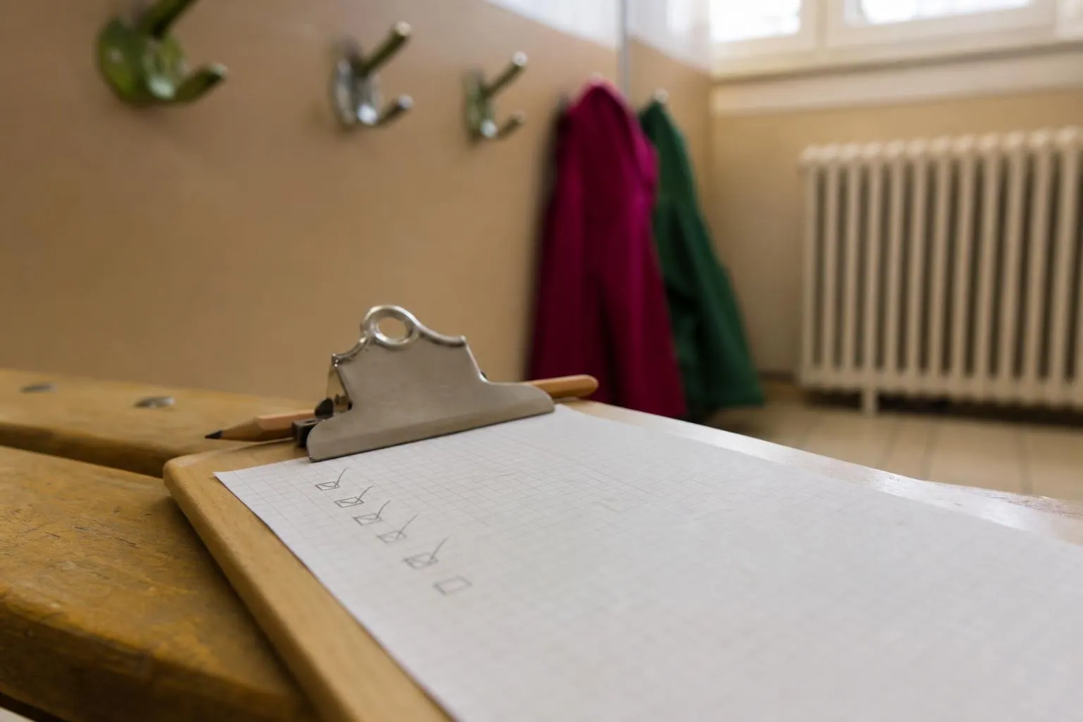 Gros plan sur une planchette à pince portant une feuille quadrillée aux cases cochées au crayon, posée sur un banc de vestiaire d’école
